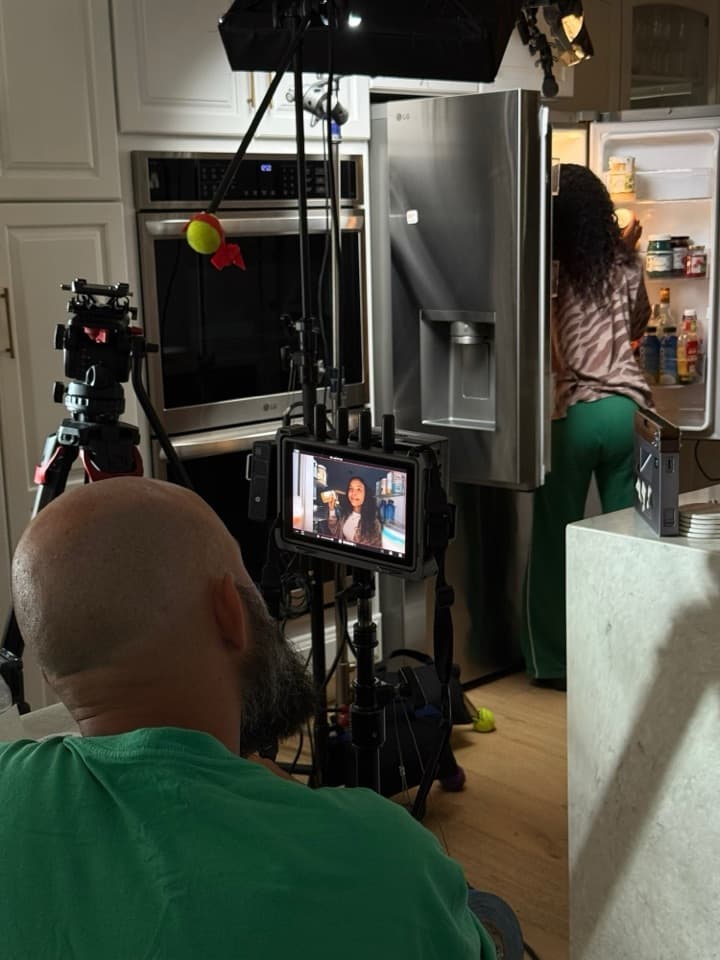 A kitchen scene: the director watches the framed shot on a monitor while the presenter reaches into the fridge.